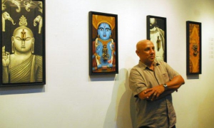 Exposición de Aristides Hernández (Ares) - Ares toca madera - Tras Ares, y a su izquierda, un Buda con una aldaba como nariz