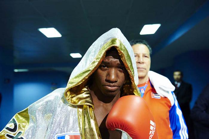 Boxeador con un puño en alto y en el fondo se ven dos personas más.