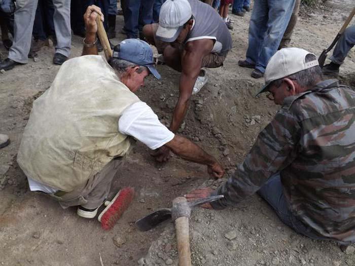 Hombres con una pala agachados explorarando un terreno.