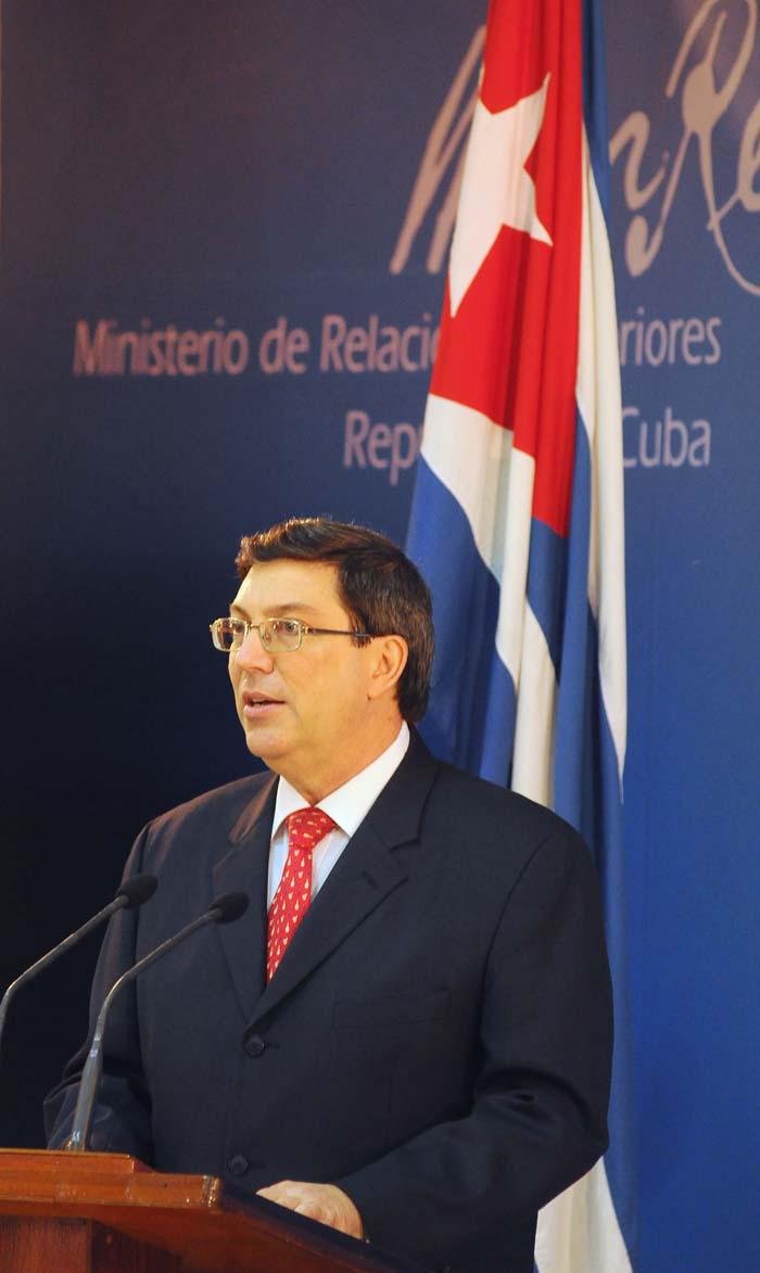 Bruno Rodríguez Parrilla hablando con la bandera cubana atrás y al fondo espacio azul donde se lee Ministerio de Relaciones Exteriores.