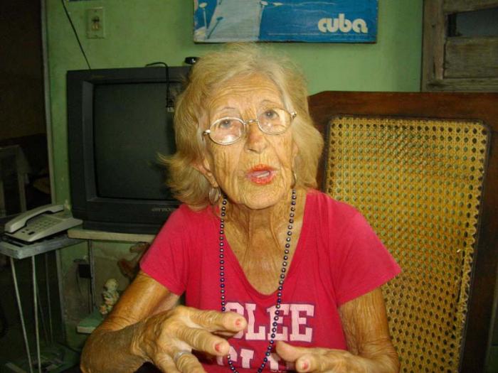 Señora mayor sentada a un sillón con pullover rojo hablando y gestionando con las manos.