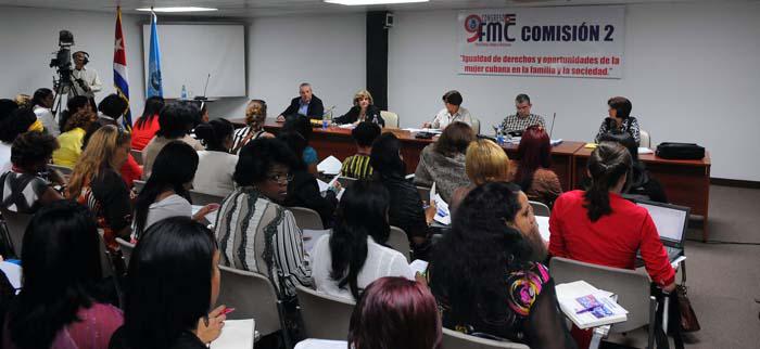 Mujeres sentadas en una sala y frente a ellas otras personas sentadas a una mesa.