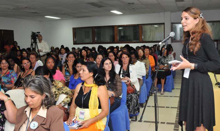 Mujeres sentadas escuchando a otra que habla a través de un micrófono.