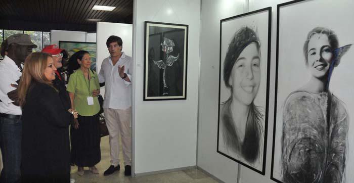 Varias personas observan una exposición en las que se pueden ver dos fotos grandes de Vilma Espín.