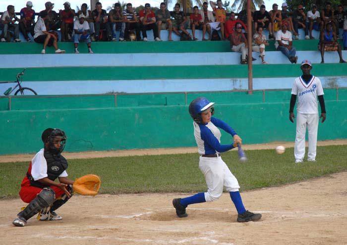 Niños jugando béisbol y al fondo personas presenciando el juego.