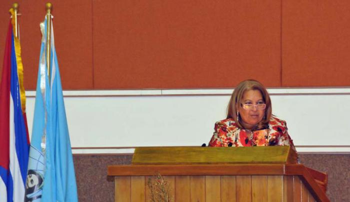 Teresa Amarelle leyendo y al lado una bandera cubana y otra de la FMC.