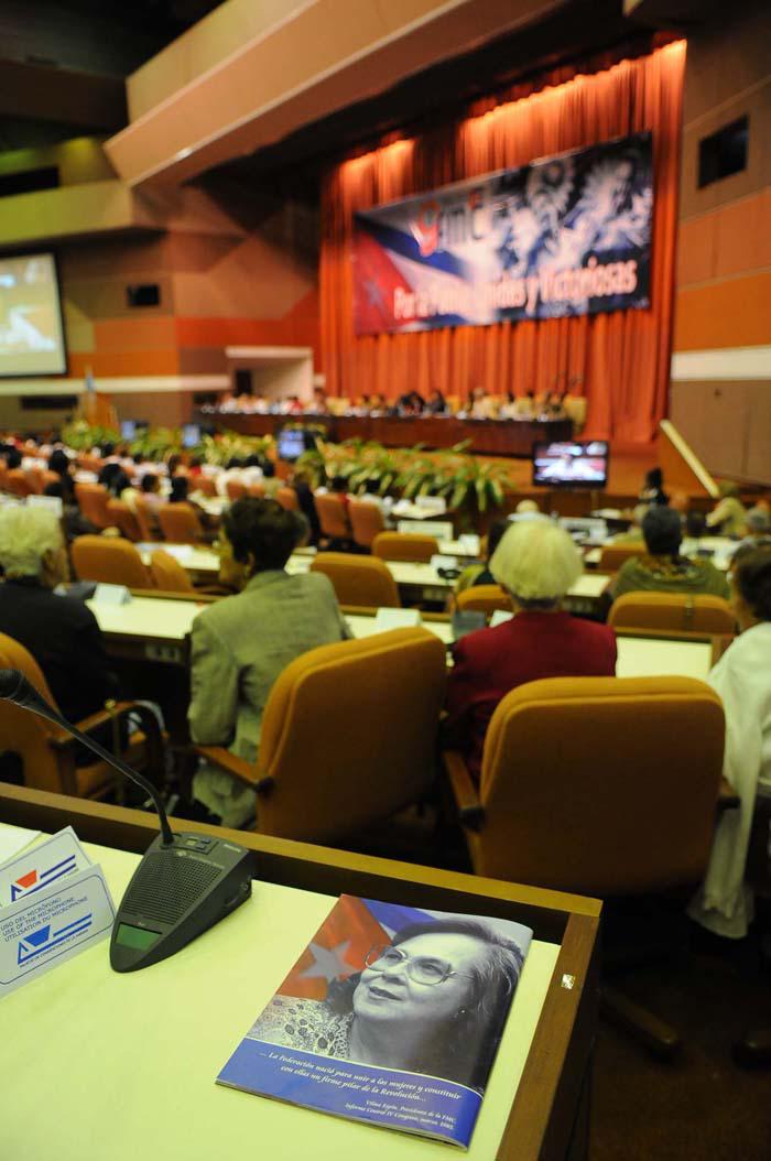 Vista general del plenario. En una mesa se ve un documento en el que aparece la imagen de Vilma Espín y la bandera cubana.