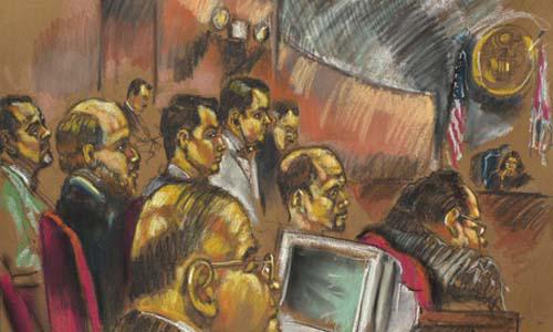 Varias personas en un juicio. La persona que primero se ve tiene una computadora frente a él, al final se ve a la jueza y al lado de ella cuelga una bandera norteamericana y otra a su izquierda.