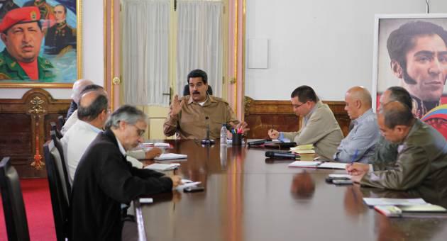 Nicolás Maduro en una mesa con otros dirigentes venezolanos, al fondo una fotografía de Hugo Chávez y de Simón Bolívar.