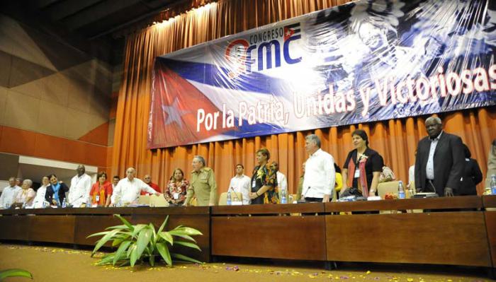 Raúl, Machado Ventura y otros dirigentes y delegadas de pie en la presidencia y atrás un cartel gigantesco que dice 9no Congreso de la FMC y en el que se lee además: 