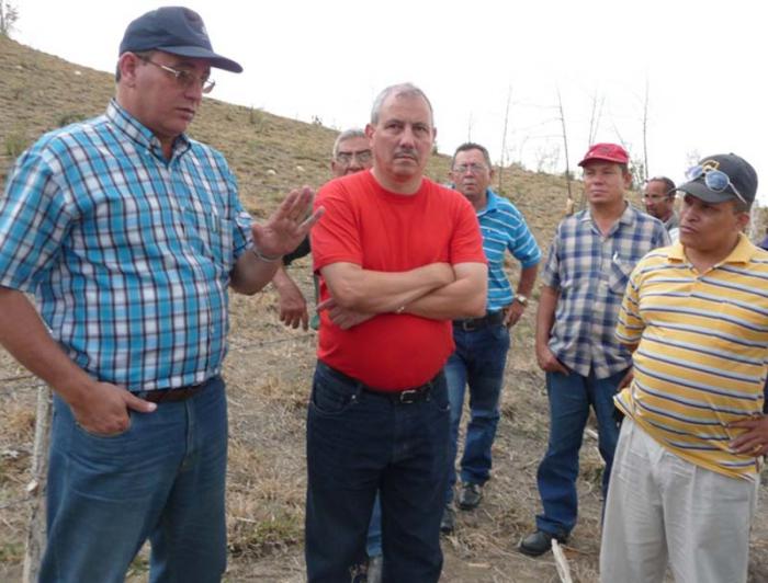 Varios hombres escuchan a uno con camisa de cuadro azul y blanca hablando.