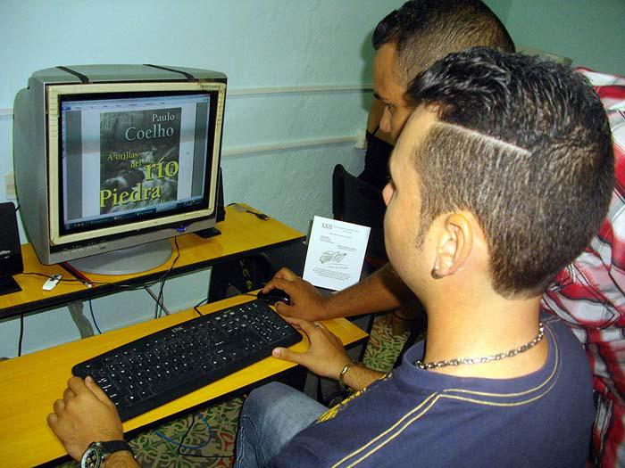 Un muchacho sentado frente a una computadora y otro de pie manipulando un mouse.