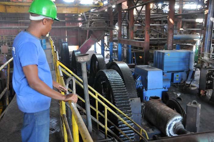 Trabajador con un casco verde que observa las máquinas de un central azucarero.