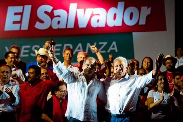 Con las manos alzadas Oscar Ortiz y Sánchez Cerén, una multitud de personas a sus espaldas y un enorme letrero rojo con letras blancas que dice El Salvador.