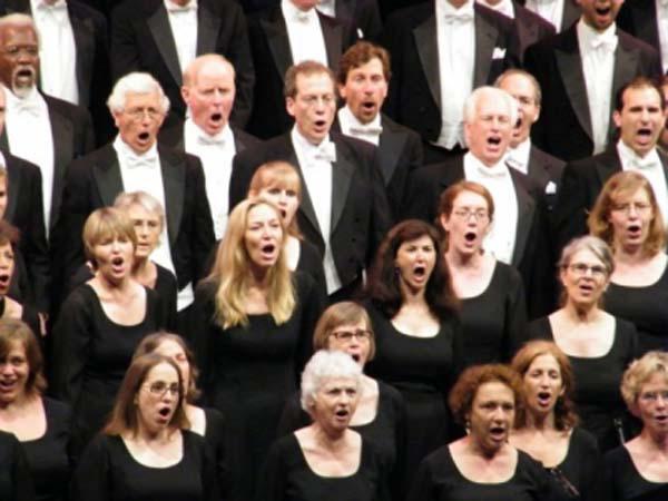 Coro de hombres y mujeres vestidos de negro cantando.