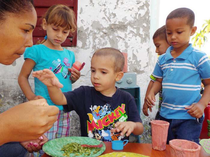 Varios niños pequeños jugando y una mujer con ellos.