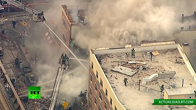 Edificio lleno de humo y bomberos tirando agua y en una azotea.
