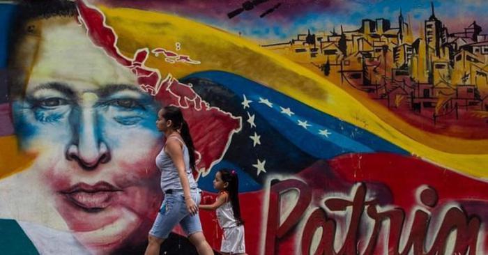 Mujer camina con su niña frente a un cartel de Chávez en Venezuela.