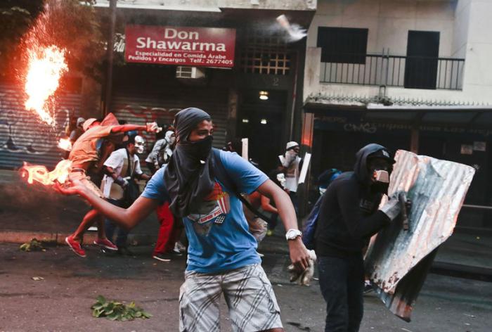 Las violentas protestas antigubernamentales de la oposición venezolana, en febrero del 2014, provocaron decenas de muertes y enormes pérdidas materiales. foto: rnv.gob.ve Un protestante enmascarado lanza un  cocktail Molotov contra la policia nacional bolivariana.