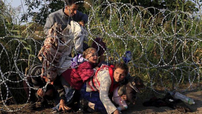 Inmigrantes sirios cruzan una cerca en la frontera de Serbia con Hungría
