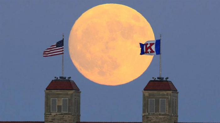 La luna se eleva más allá de banderas en lo alto Fraser Hall en el campus de la Universidad de Kansas en Lawrence.