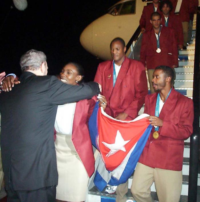 Fidel abraza a Mireya Luis, capitana del equipo Cuba, al regreso de la delegación de los Juegos de Sidney 2000, donde el voli (f) ganó su tercera presea de oro olímpica consecutiva. A la derecha, el saltador Iván Pedroso, y detrás el boxeador Félix Savón.