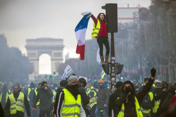 Una mujer, parte de los chalecos amarillos, grita consignas subida a un semáforo durante una protesta en los Campos Elíseos en París. FOTO: EFE