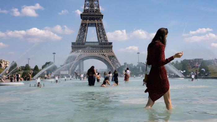 Una mujer se refresca con el agua de la fuente de la Plaza del Trocadero, frente a la Torre Eiffel, durante la ola de calor que recorre París (Ian Langsdon / EFE)