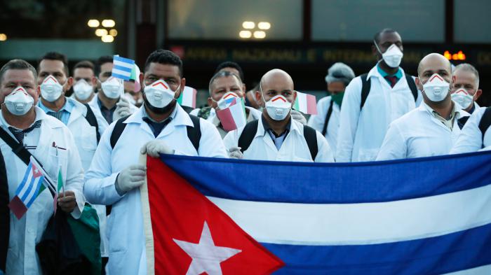 Medics and paramedics from Cuba pose upon arrival at the Malpensa airport of Milan, Italy, Sunday, March 22, 2020. 53 doctors and paramedics from Cuba arrived in Milan to help with coronavirus treatment in Crema. For most people, the new coronavirus causes only mild or moderate symptoms. For some it can cause more severe illness, especially in older adults and people with existing health problems. (AP Photo/Antonio Calanni)