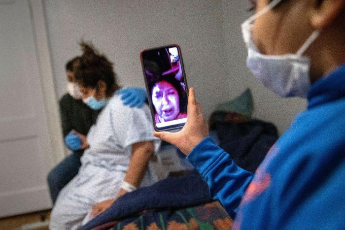 Junior, de 7 años, le permite a su abuela mirar en una video llamada, mientras su madre Zully, quien padece Covid-19, y su padre Marvin se abrazan después de que Zully regreso a casa del hospital. 