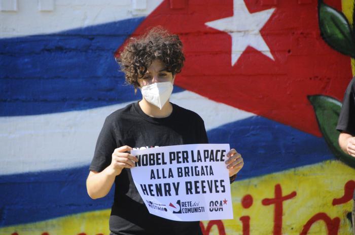 Jóvenes italianos, formados en silencio, inmóviles por unos minutos, frente al mural, sostienen carteles que demandan sus deseos de premiar a los cubanos. 