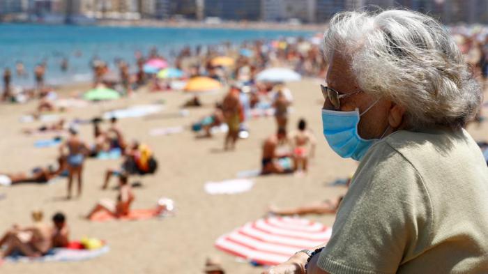 Una mujer protegida con una mascarilla observa a los bañistas deLas Canteras,una de las playas de Las Palmas de Gran Canaria.