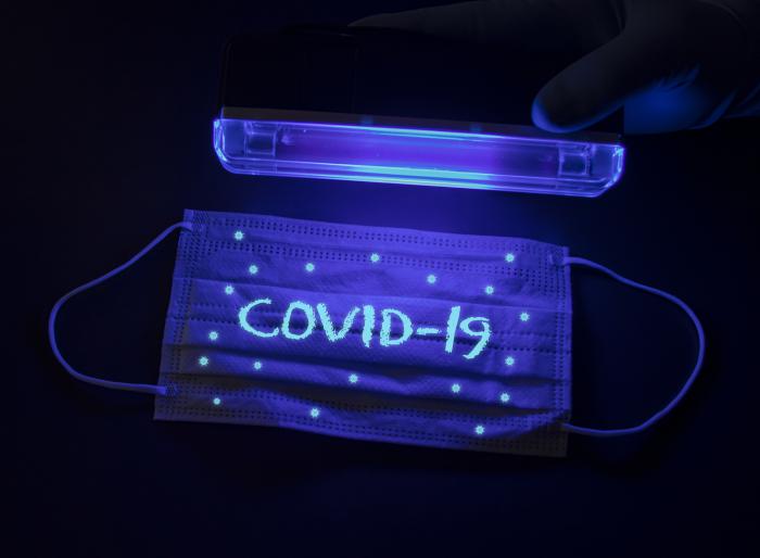Protective medical mask with the inscription Covid-19 and with small coronavirus molecules under an ultraviolet lamp