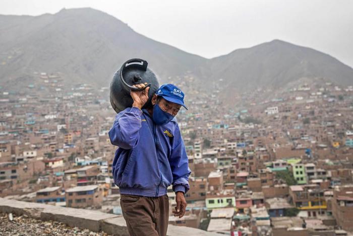 Peruvian self-employed gas delivery man Hipolito Rosales, a migrant living and servicing residents in the heights of the Vista Alegre shantytown of the Comas district, in the outskirts of Lima, climbs a hill to deliver a 27-kilogram (60 lbs) propane tank, commonly used for cooking stoves and heating, to a home that requested the service via mobile phone on May 21, 2020. - Mandatory social isolation dictated by Peruvian President Martin Vizcarra since March 16, has forced many residents in these impoverished areas to rely on the self-enterprising to fulfill their food and other basic necessities in areas where danger of contagion of the novel coronavirus is high due to the closeness among homes and health conditions. Peru crossed the 100 thousand confirmed cases and statistics stand as of May 21 on 108,769 infected, of which 43,587 have recovered and 3,148 have died since the virus was first detected in Peru on March 6. (Photo by GERALDO CASO / AFP)