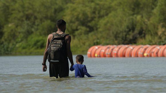 Migrantes junto a grandes boyas en el Río Grande, en Eagle Pass, Texas.