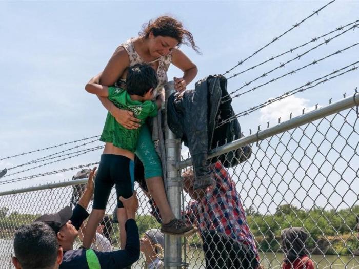 Una madre ayuda a su hijo a cruzar la cerca de alambre de púas en Eagle Pass, Texas, después de cruzar a Estados Unidos desde México. Foto: AFP